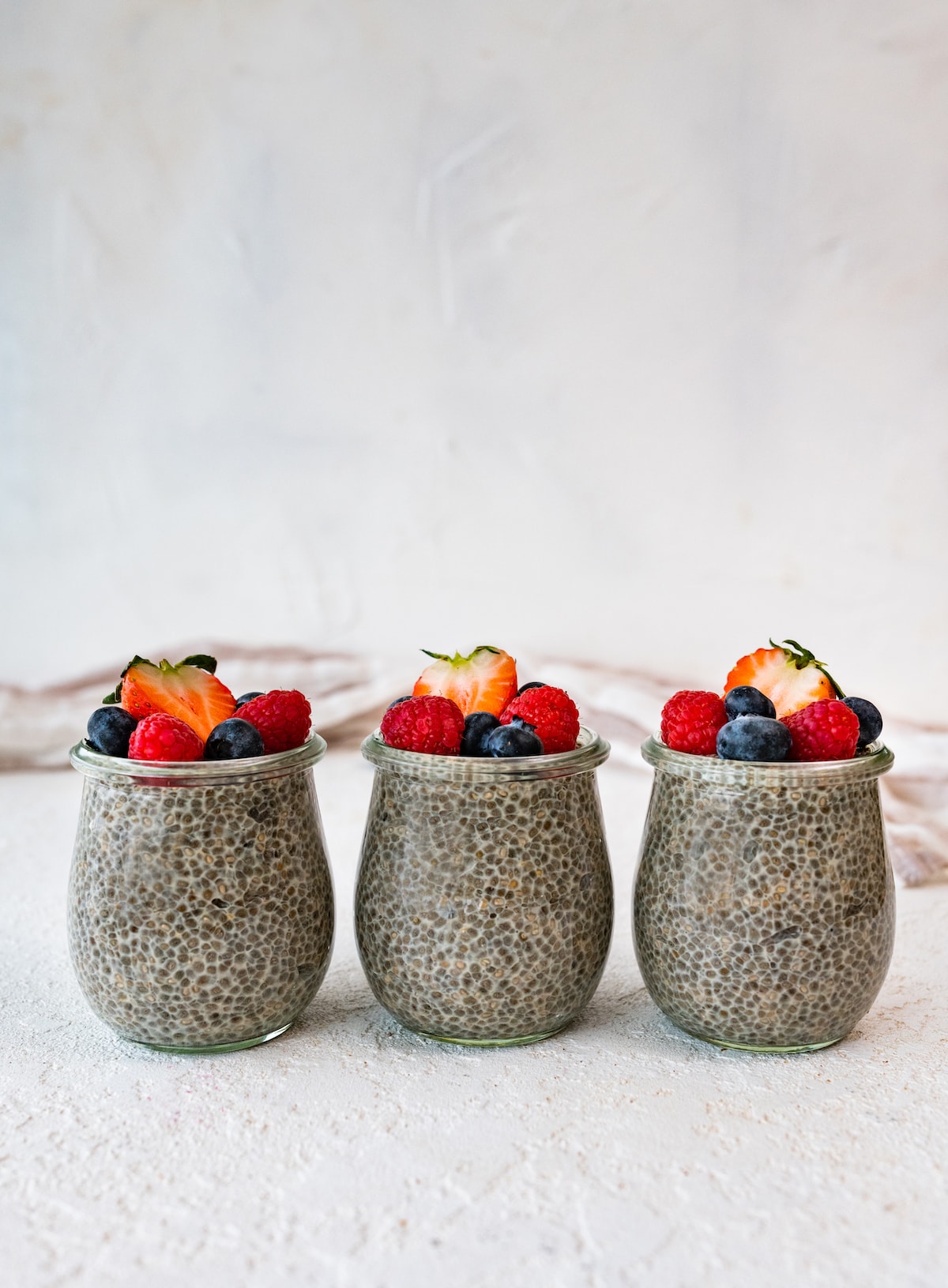 Three glass cups of chia pudding topped with fresh berries.