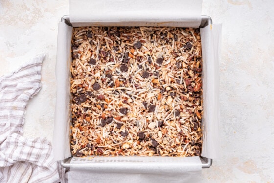 Chocolate coconut bars in a square baking dish with a golden crisp topping after being baked.