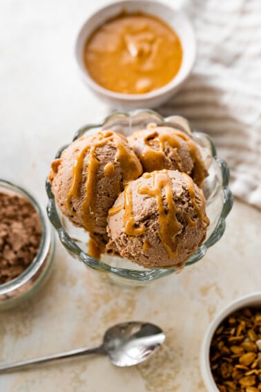 Chocolate peanut butter protein icee cream scooped in an ice cream bowl drizzled with peanut butter.