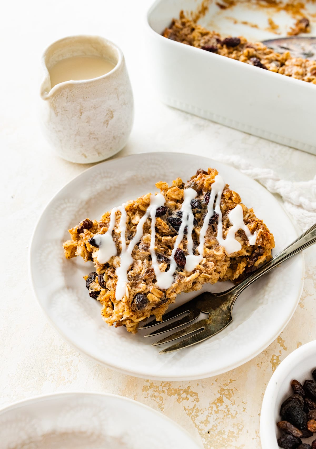 A serving of cinnamon raisin baked oatmeal on a small plate with a drizzle of coconut butter on top.