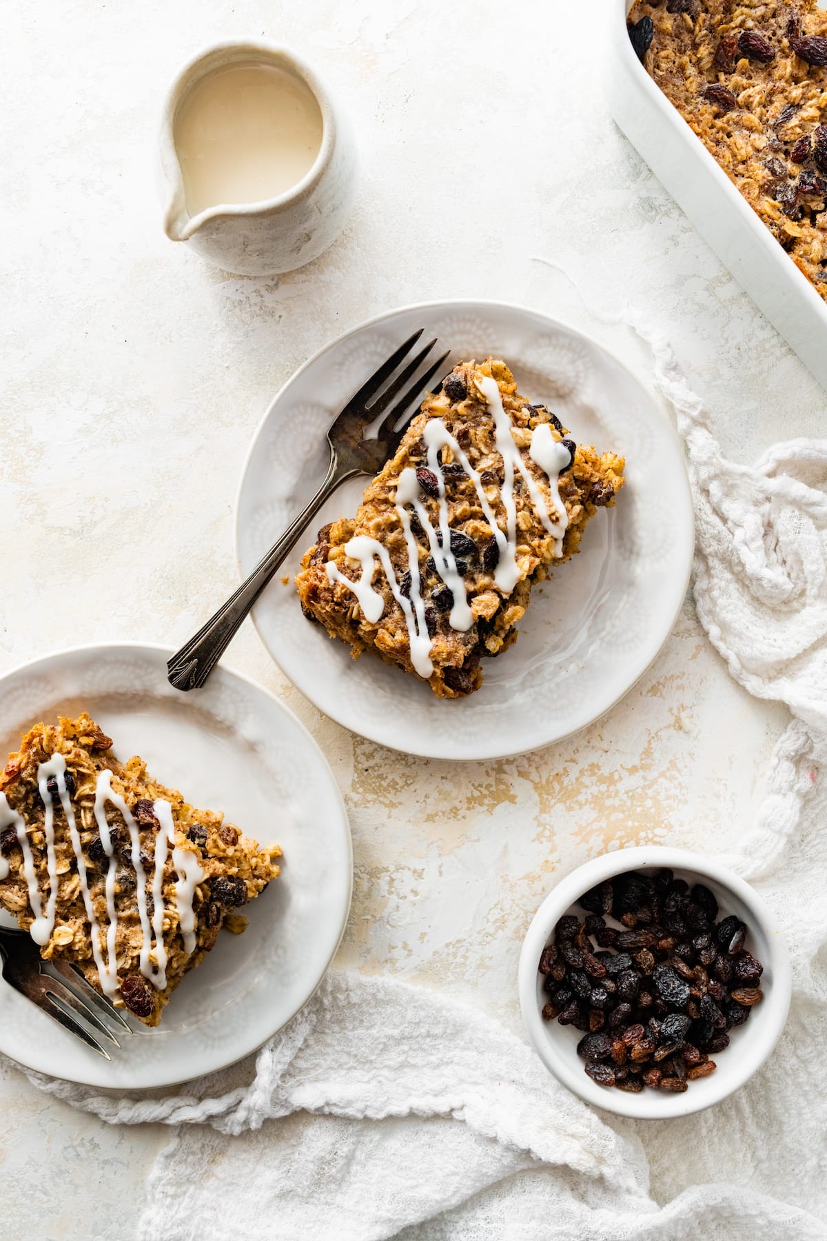 Two servings of cinnamon raisin baked oatmeal on small plates with a drizzle of coconut butter on top.