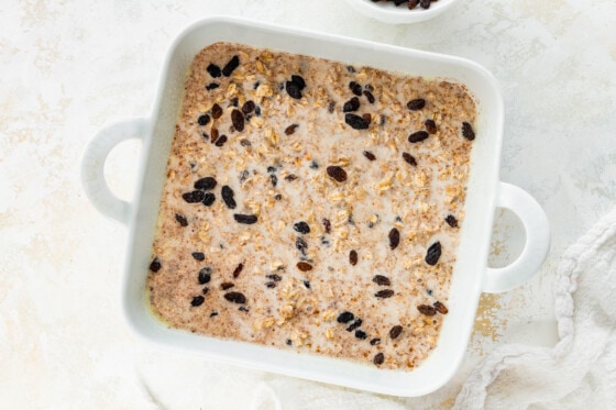 Extra raisins are added to the cinnamon raisin baked oatmeal in a square baking dish before being baked.