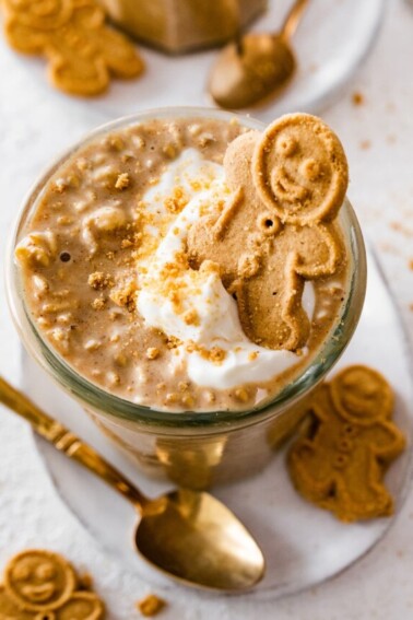 Gingerbread overnight oats in a glass cup. The overnight oats are topped with a dollop of whipped cream and a small gingerbread man.
