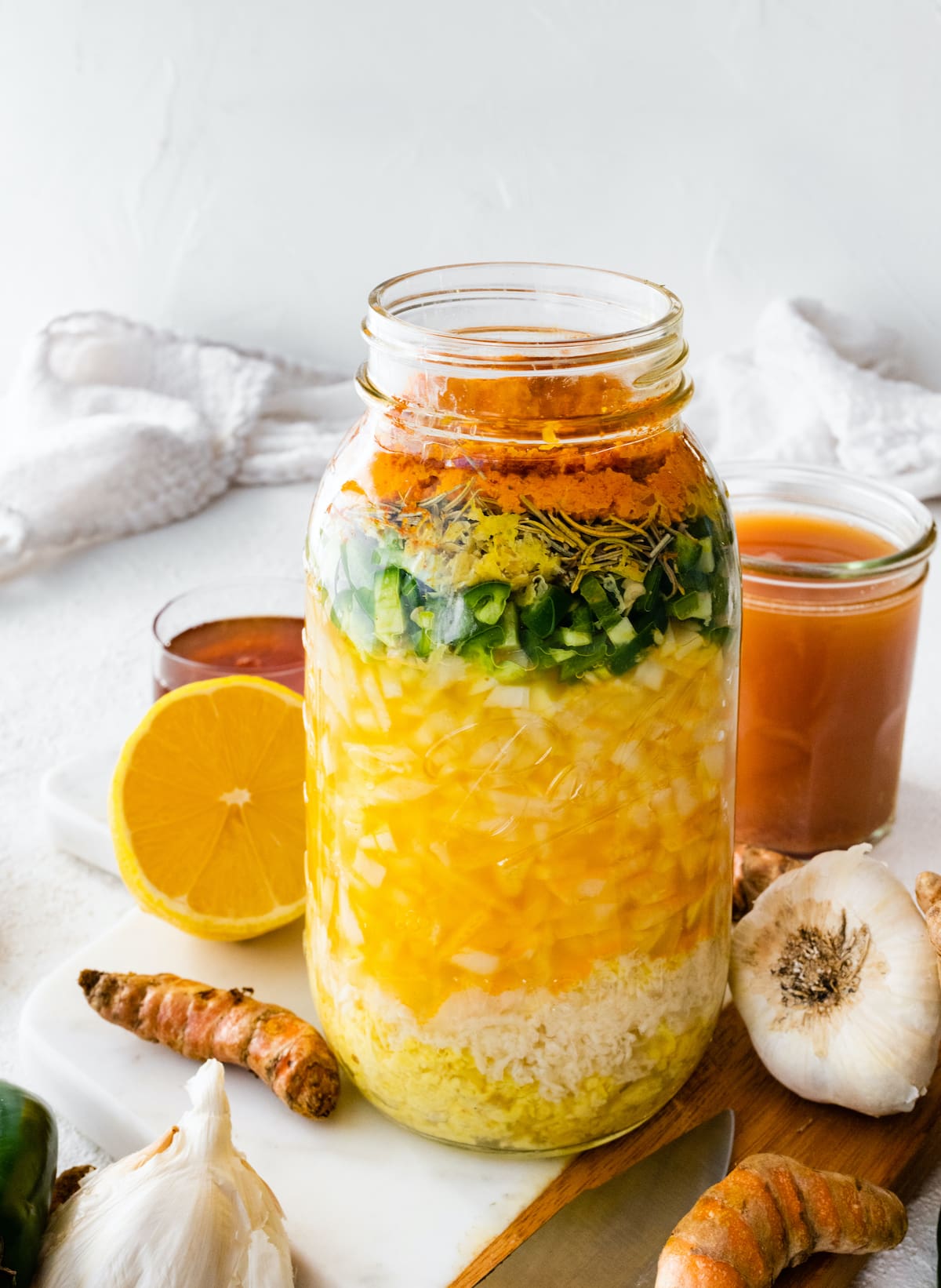 A large mason jar filled with all the ingredients used for a fire cider. Ingredients include horseradish, ginger, garlic, onions, cayenne, apple cider vinegar, and honey.