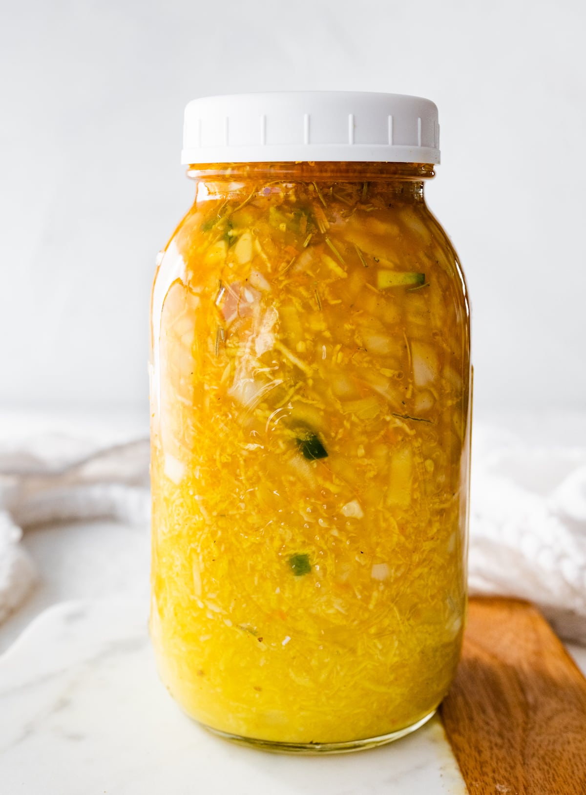 A large mason jar filled with all the ingredients used for a fire cider. Ingredients include horseradish, ginger, garlic, onions, cayenne, apple cider vinegar, and honey.