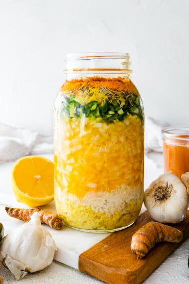 A large mason jar filled with all the ingredients used for a fire cider. Ingredients include horseradish, ginger, garlic, onions, cayenne, apple cider vinegar, and honey.