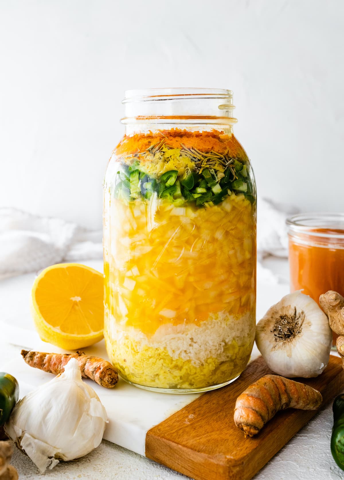 A large mason jar filled with all the ingredients used for a fire cider. Ingredients include horseradish, ginger, garlic, onions, cayenne, apple cider vinegar, and honey.