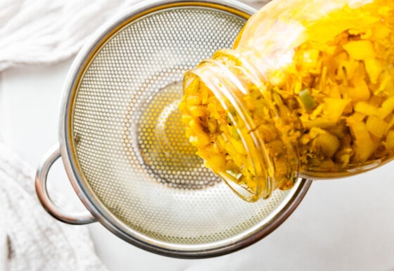 Ingredients for the apple cider being strained from a large mason jar.