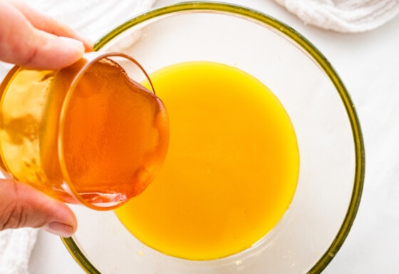 Honey being poured into a large glass bowl of fire cider.