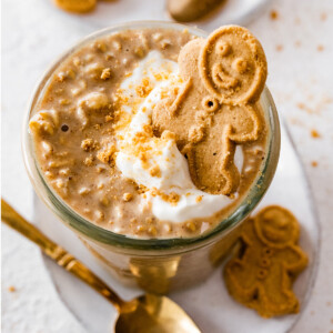 Gingerbread overnight oats in a glass cup. The overnight oats are topped with a dollop of whipped cream and a small gingerbread man.