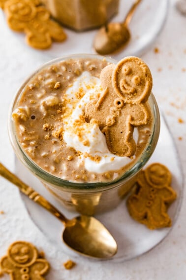 Gingerbread overnight oats in a glass cup. The overnight oats are topped with a dollop of whipped cream and a small gingerbread man.