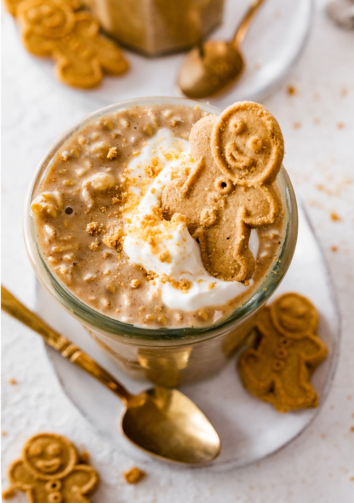Gingerbread overnight oats in a glass cup. The overnight oats are topped with a dollop of whipped cream and a small gingerbread man.
