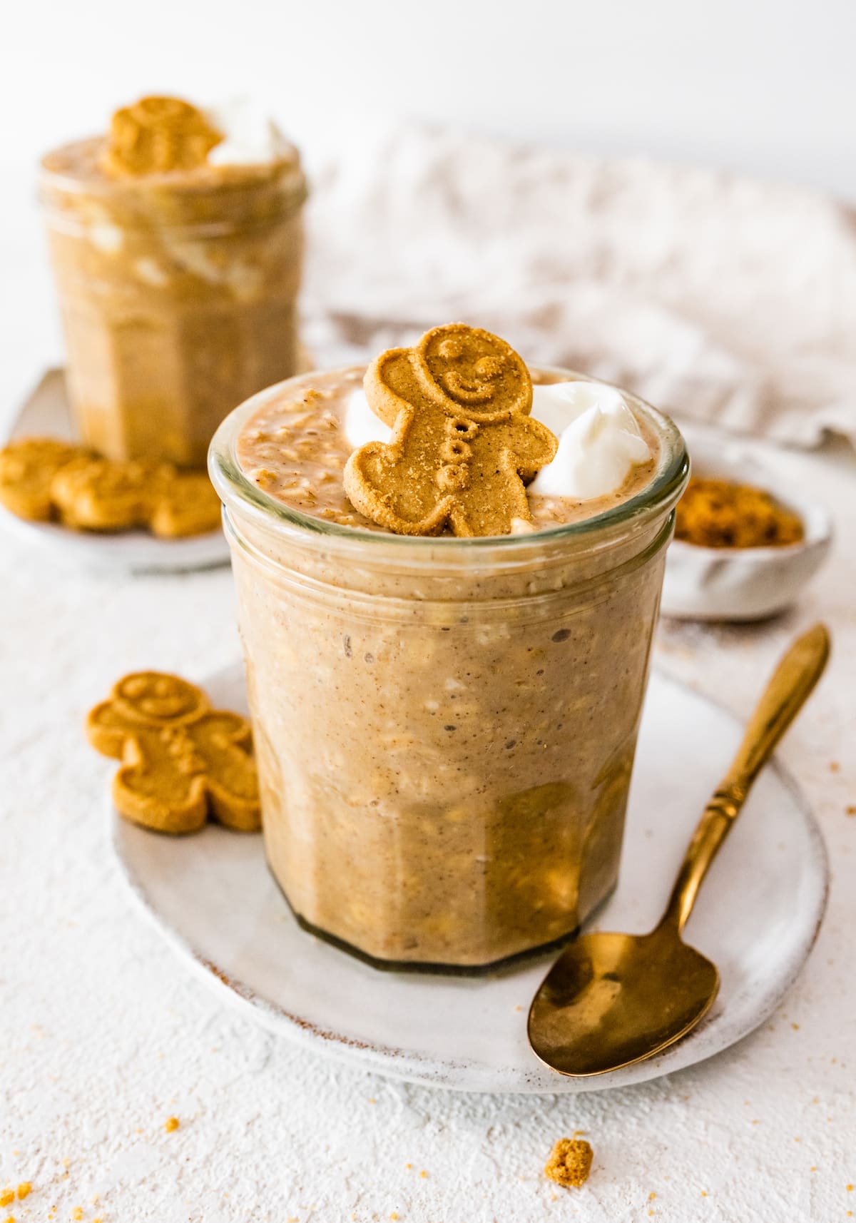 Gingerbread overnight oats in a glass cup. The overnight oats are topped with a dollop of whipped cream and a small gingerbread man.