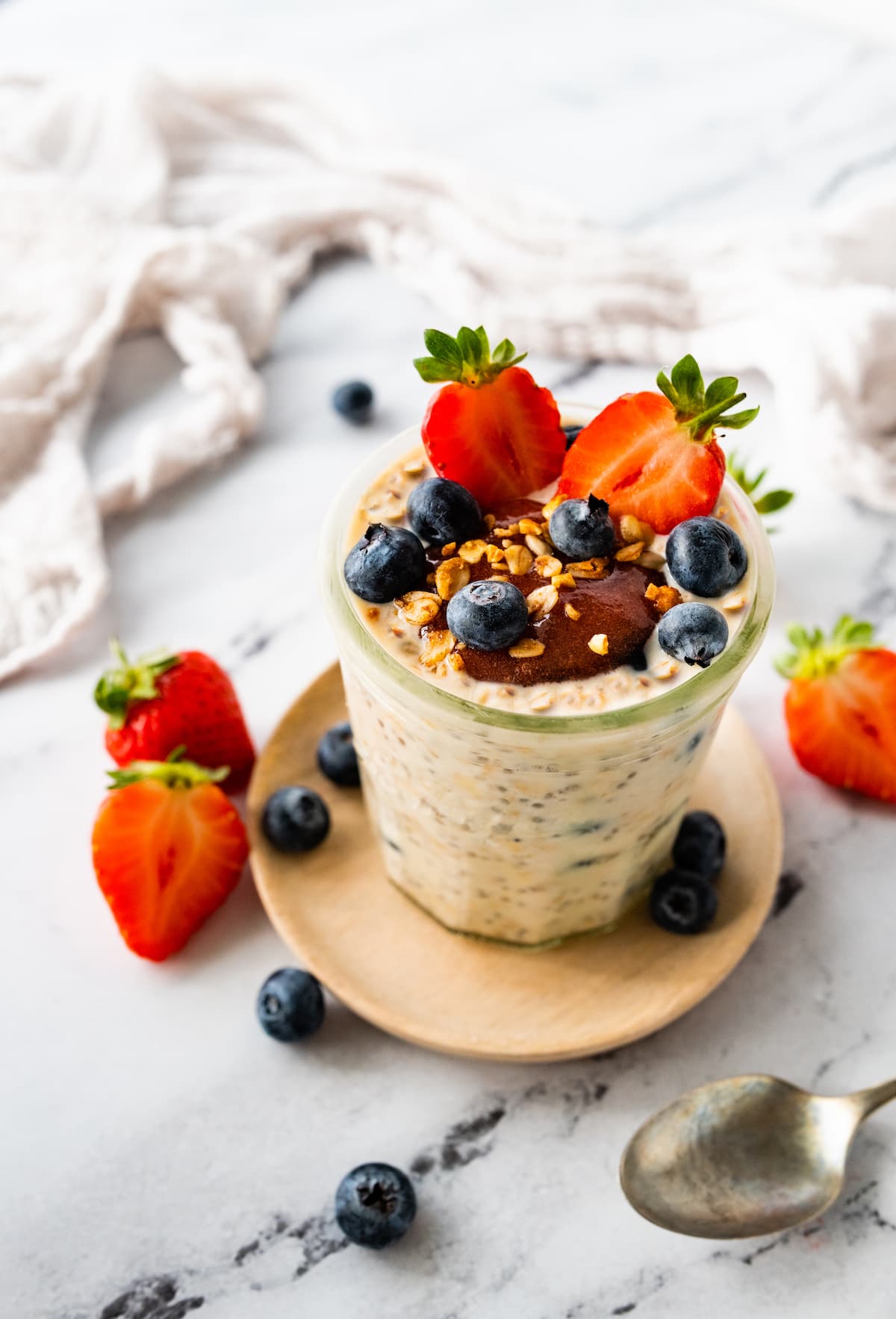 Overnight oats in a glass jar topped with fresh berries, nut butter, and nuts.
