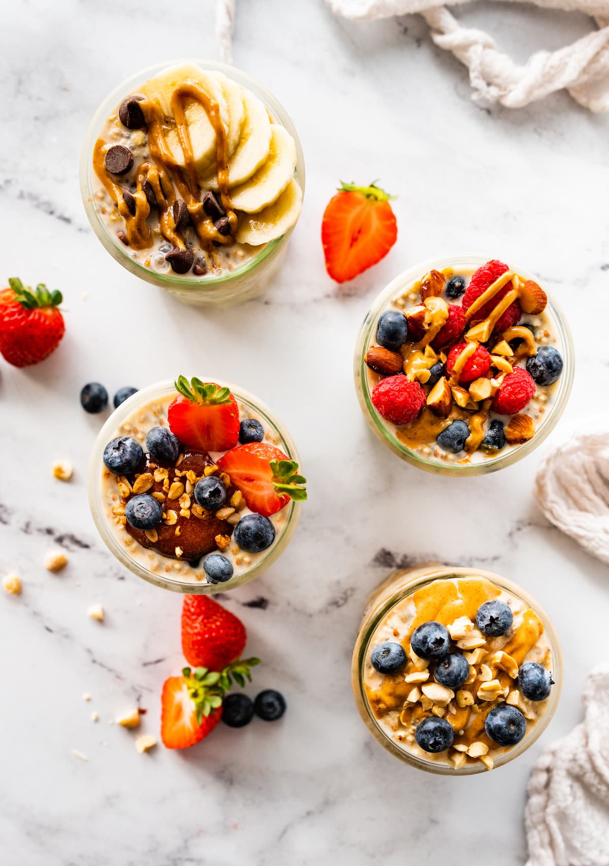 Four glass jars with overnight oats. The oats are topped with fresh berries and nut butter.