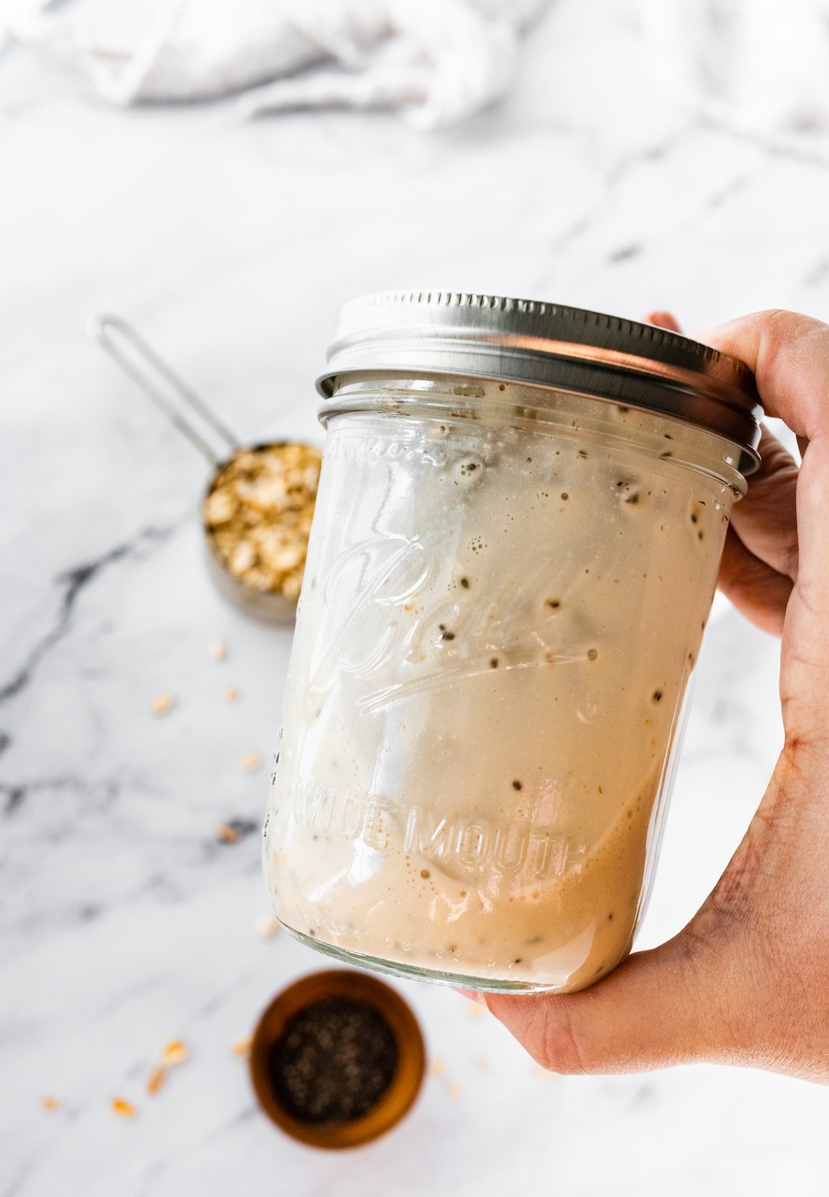 A hand shaking a sealed mason jar with overnight oats.