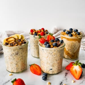 Four glass jars with overnight oats. The oats are topped with fresh berries and nut butter.