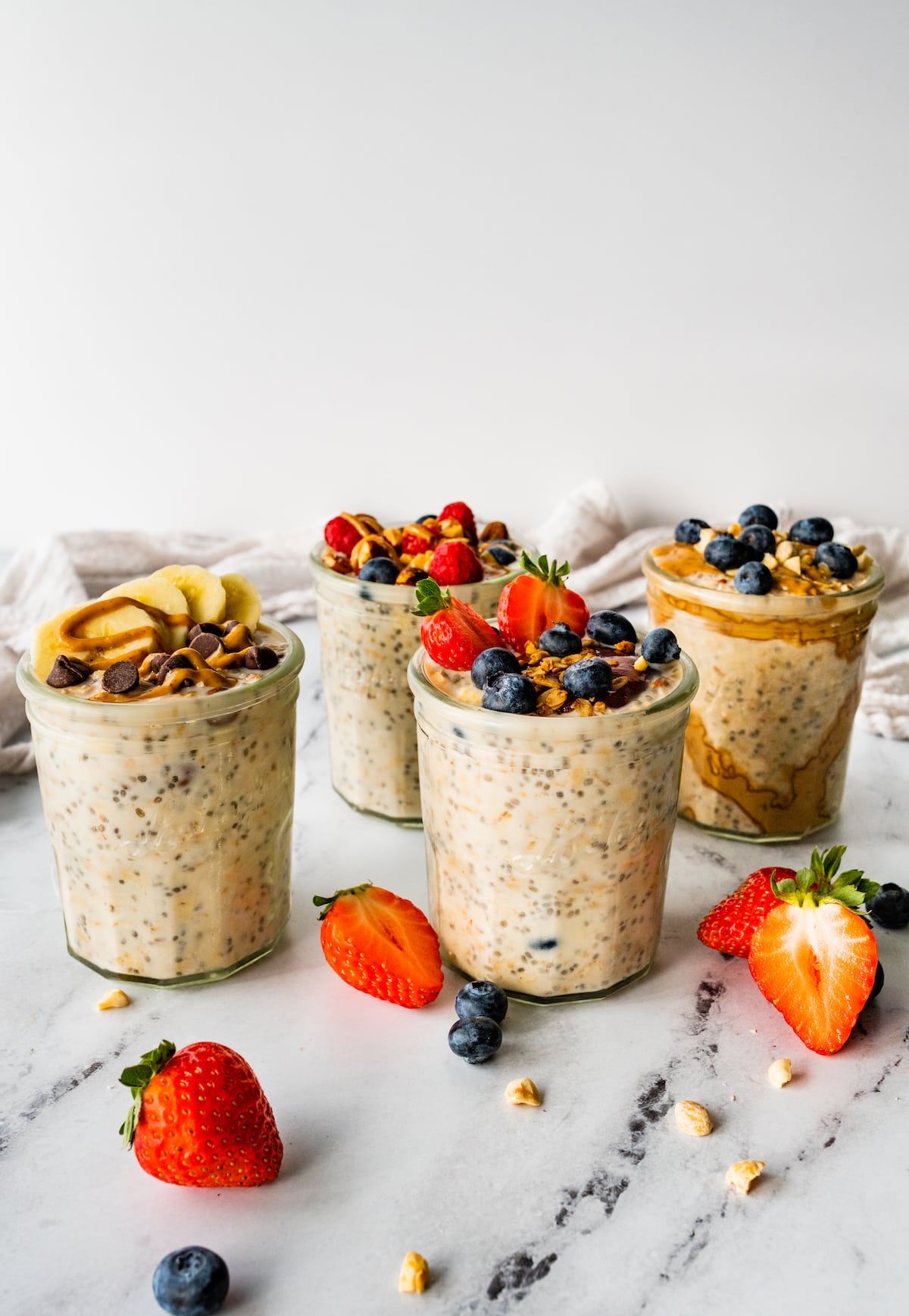 Four glass jars with overnight oats. The oats are topped with fresh berries and nut butter.
