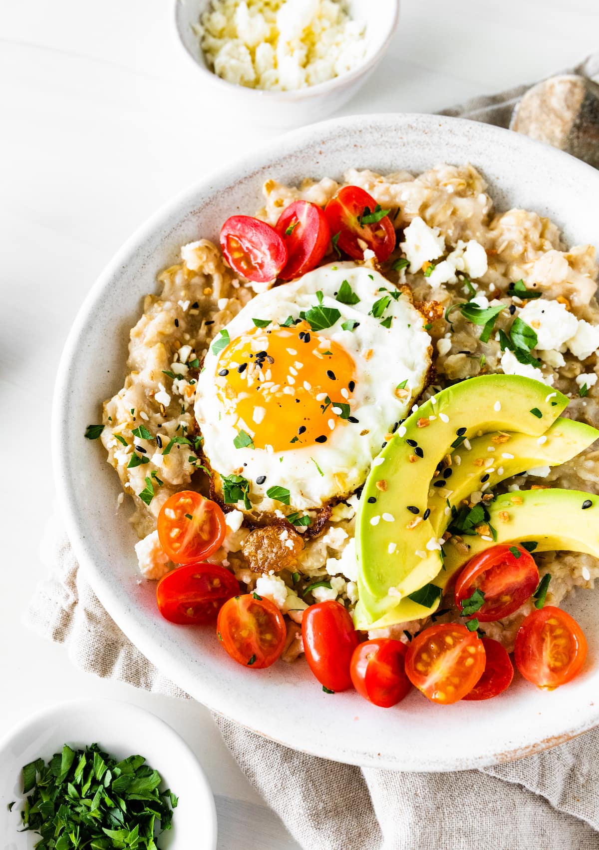 Bowl of oatmeal topped with an egg, tomatoes, avocado, feta and everything bagel seasoning.