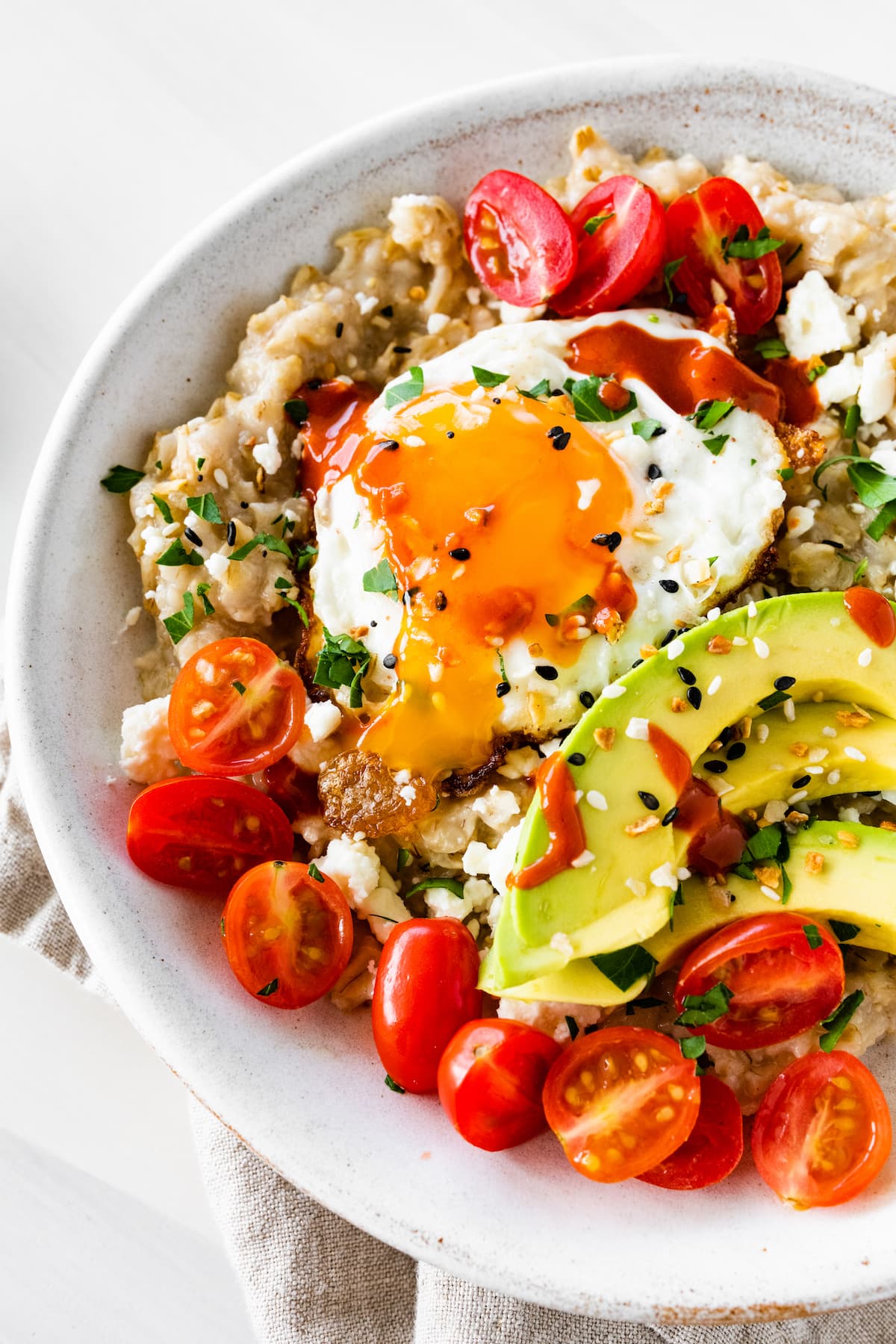 Bowl of oatmeal topped with an egg, tomatoes, avocado, feta and everything bagel seasoning.