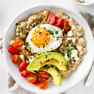 Bowl of oatmeal topped with an egg, tomatoes, avocado, feta and everything bagel seasoning.