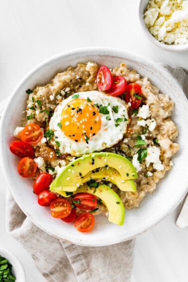 Bowl of oatmeal topped with an egg, tomatoes, avocado, feta and everything bagel seasoning.