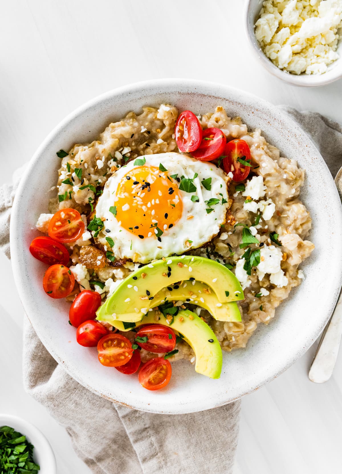 Bowl of oatmeal topped with an egg, tomatoes, avocado, feta and everything bagel seasoning.