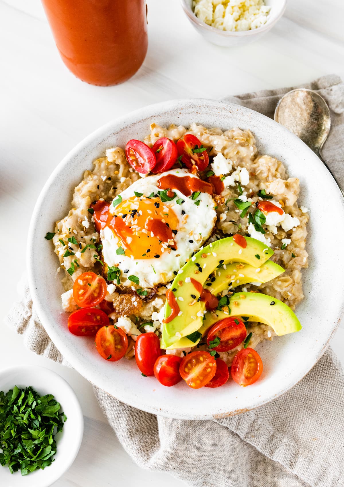 Bowl of oatmeal topped with an egg, tomatoes, hot sauce, avocado, feta and everything bagel seasoning.