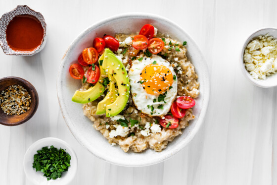 Bowl of oatmeal topped with an egg, tomatoes, avocado, feta and everything bagel seasoning.