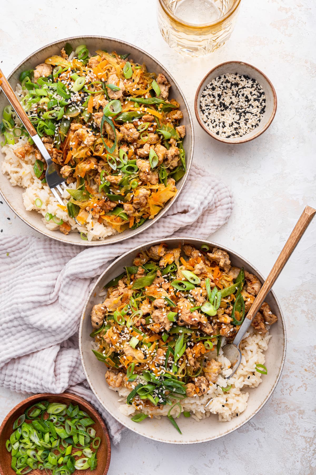 Two bowls of the tamari ground turkey skillet served with white rice and topped with green onions and sesame seeds.