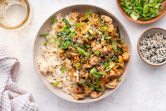 Assembled tamari ground turkey skillet served over rice in a bowl and topped with green onions and sesame seeds.