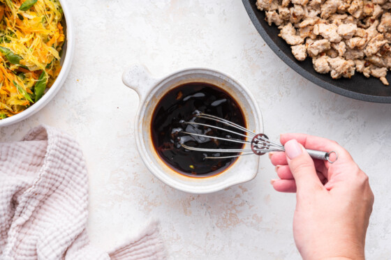 A woman's hand whisking together the sauce for the tamari ground turkey skillet.