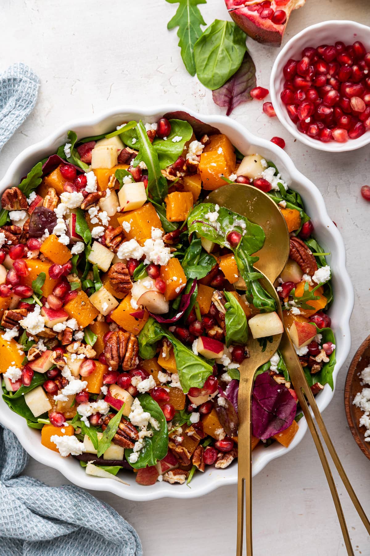 Winter salad being served in a white bowl with gold serving spoons.