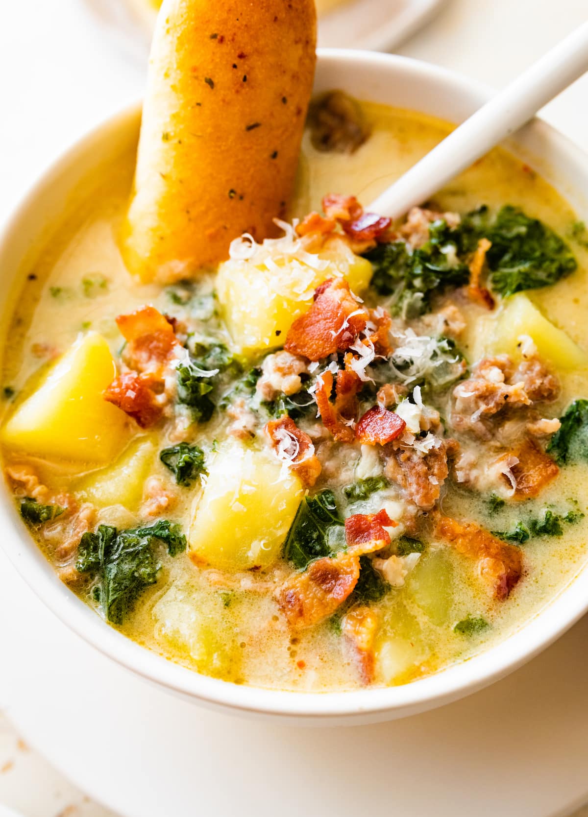 Zuppa toscana soup in a white bowl with a spoon and a roll of bread inside the soup.