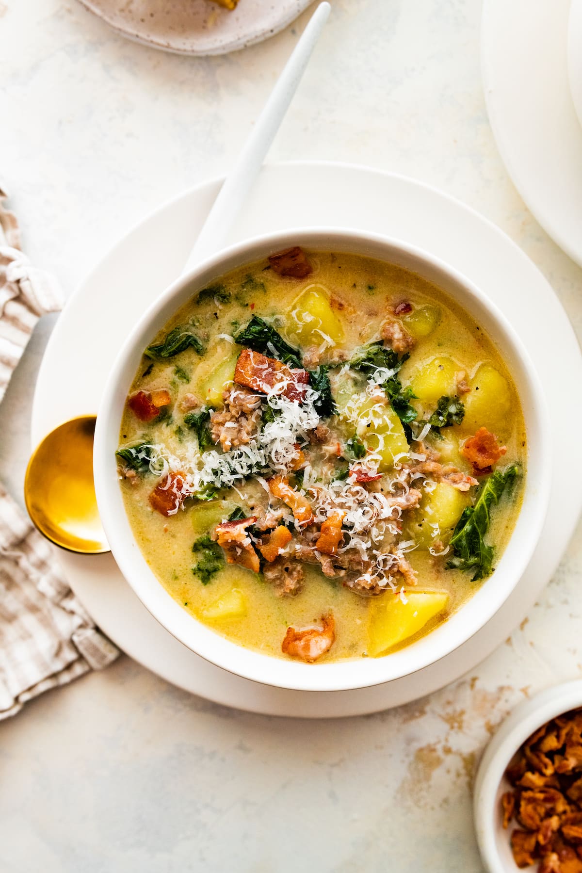 A white bowl with zuppa toscana soup on a plate.