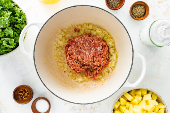 Ground italian sausage added to the sauteed onions in a pot.