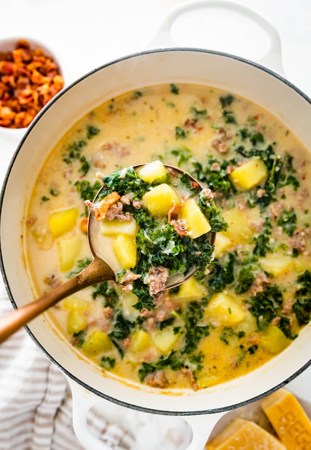 A serving spoon with a small portion of zuppa toscana soup over a large pot of the soup.