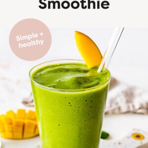 Green Smoothie in a glass garnished with a mango slice and glass straw.