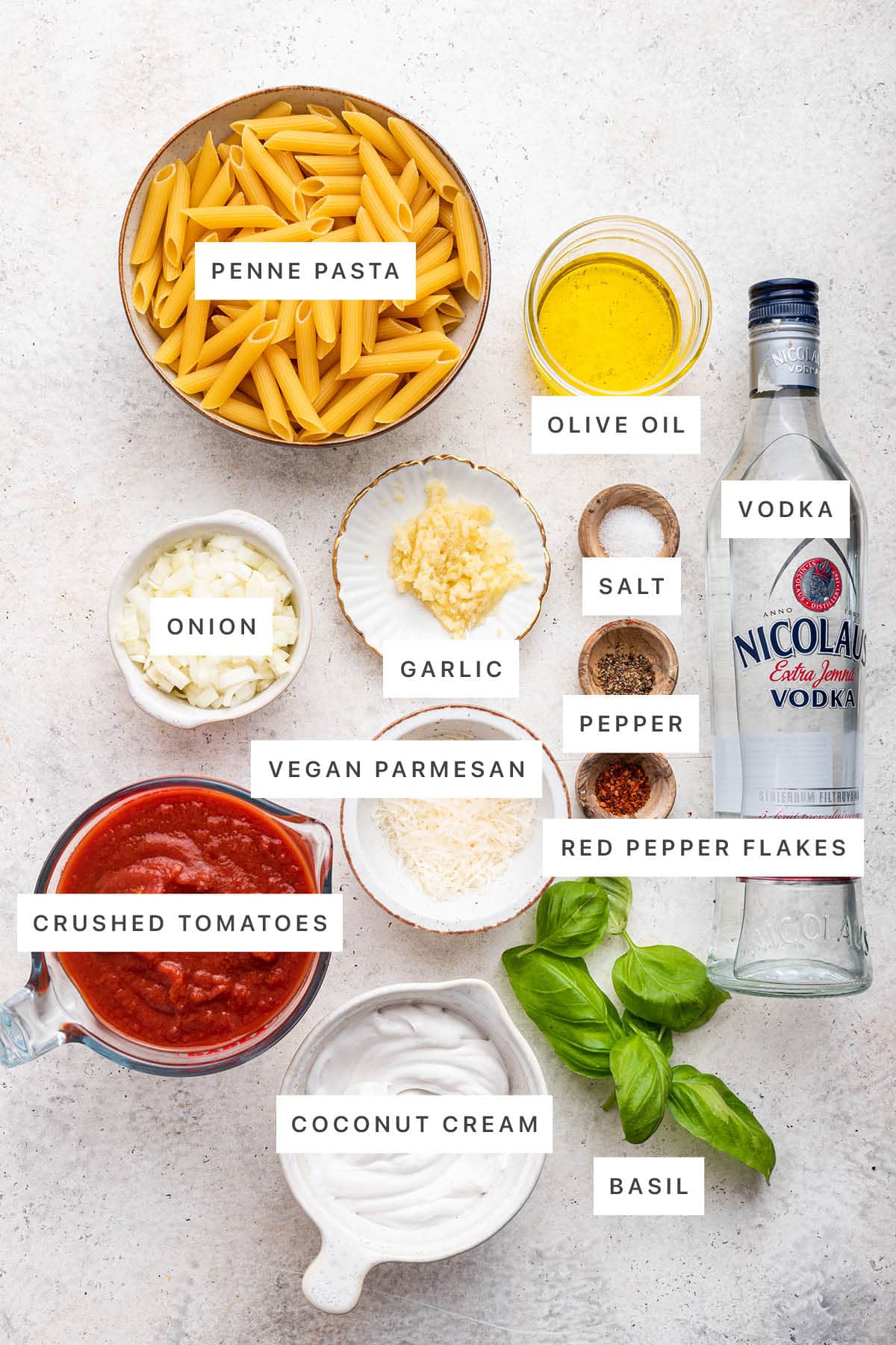 Ingredients measured out to make Penne alla Vodka: penne, olive oil, vodka, onion, garlic, salt, pepper, red pepper flakes, parmesan, crushed tomatoes, coconut cream and basil.