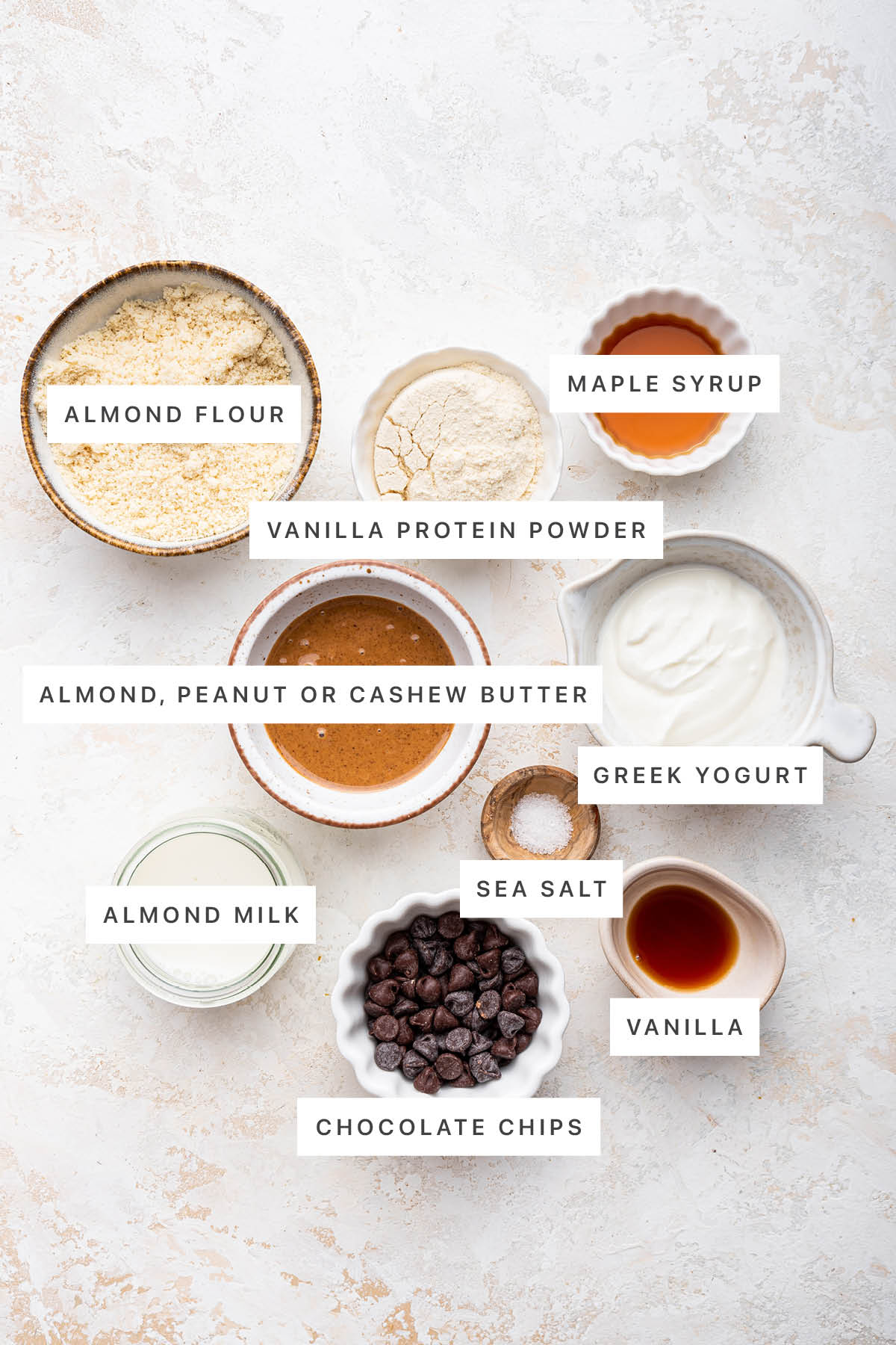 Ingredients measured out to make Protein Cookie Dough: almond flour, vanilla protein powder, maple syrup, almond/cashew/peanut butter, Greek yogurt, almond milk, sea salt, vanilla and chocolate chips.