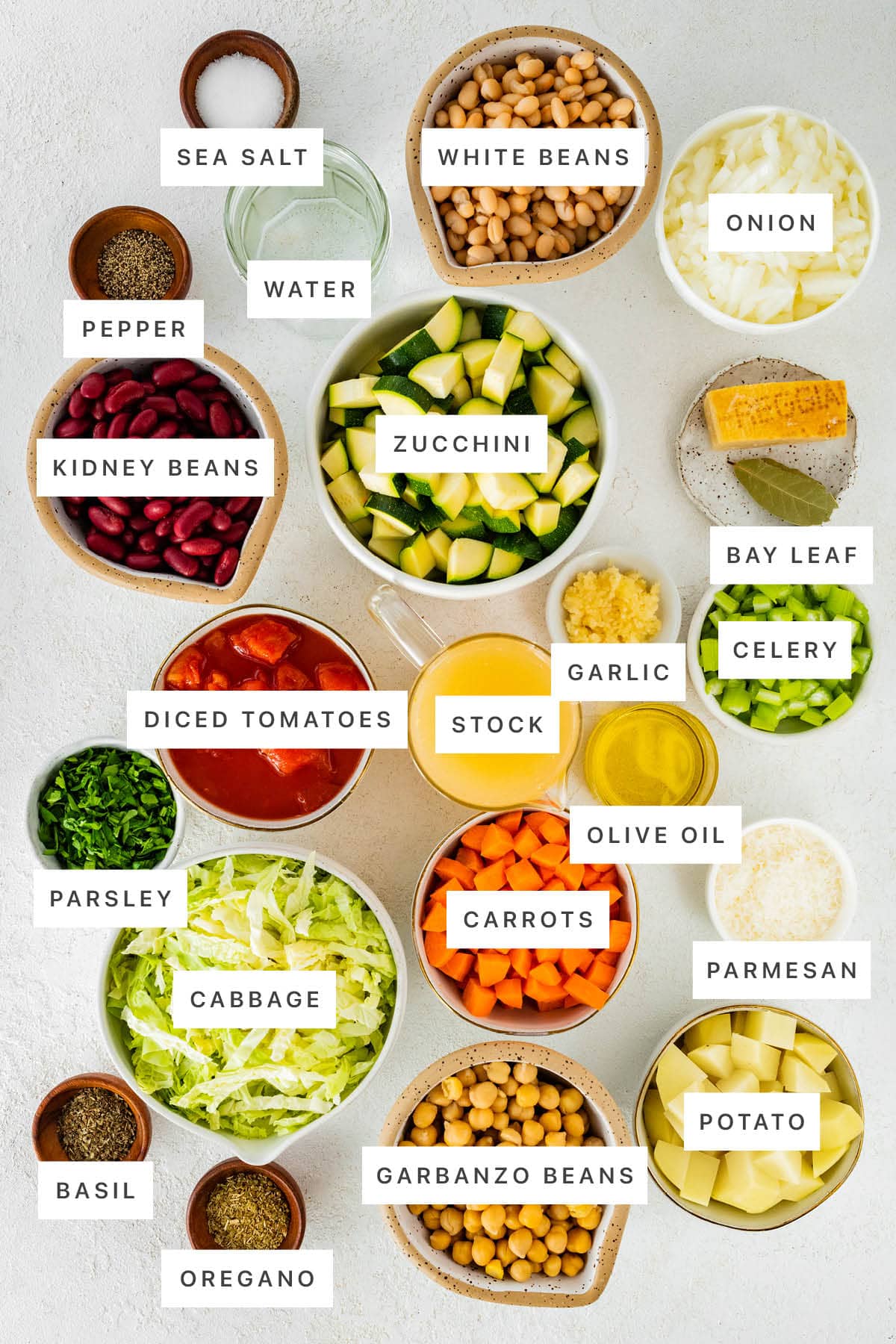 Ingredients measured out to make Slow Cooker Minestrone Soup: sea salt, pepper, water, white beans, onion, kidney beans, zucchini, bay leaf, diced tomatoes, stock, garlic, celery, olive oil, parsley, cabbage, carrots, parmesan, basil, oregano, garbanzo beans and potato.