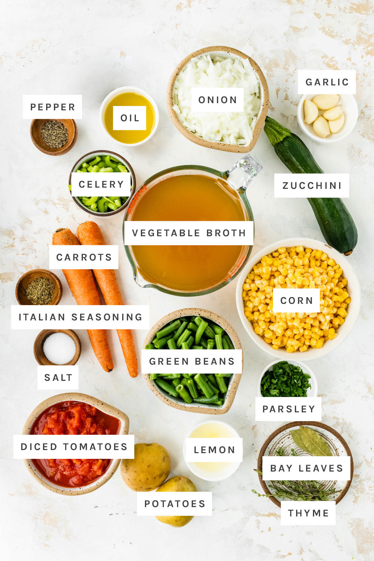Ingredients measured out to make vegetable soup: pepper, oil, onion, garlic, celery, vegetable broth, zucchini, carrots, Italian seasoning, corn, salt, green beans, parsley, diced tomatoes, potatoes, lemon, bay leaves and thyme.