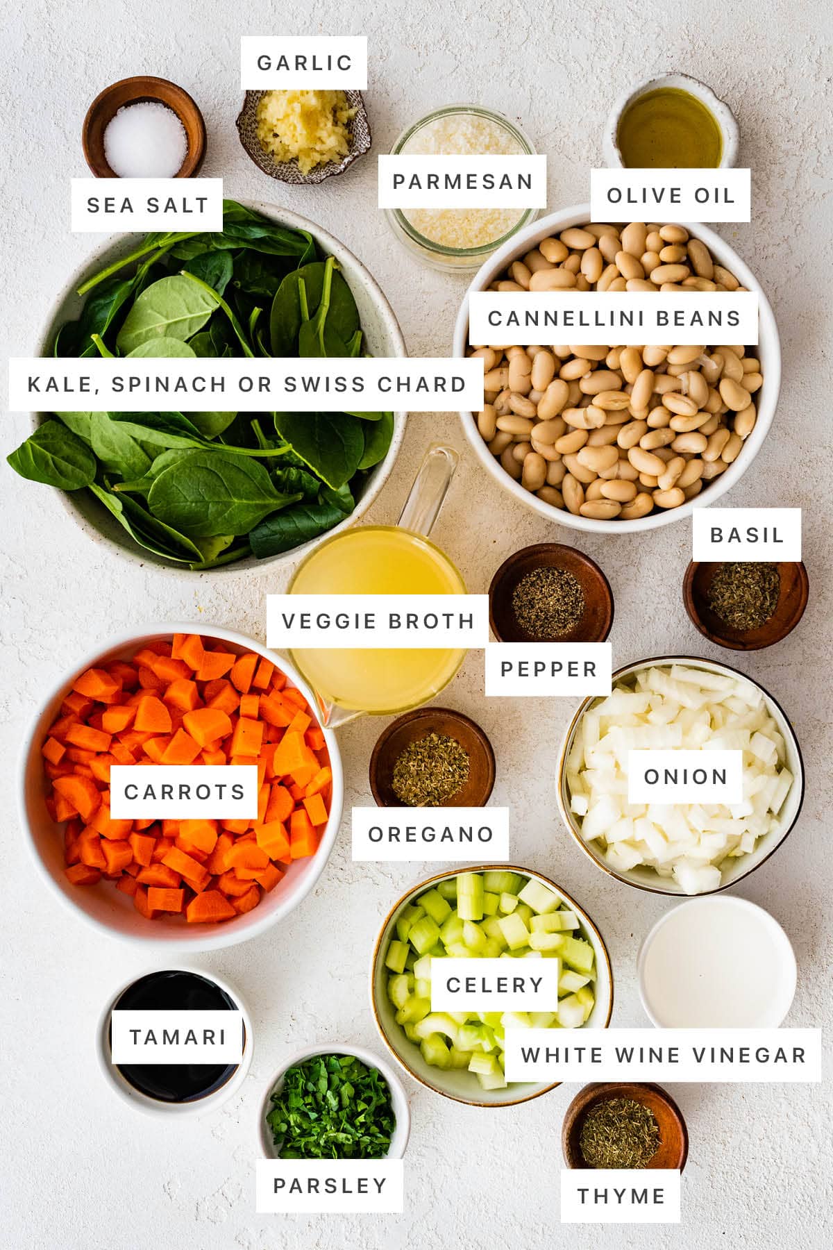 Ingredients measured out to make Mediterranean White Bean Soup: sea salt, garlic, parmesan, olive oil, cannellini beans, spinach, veggie broth, pepper, basil, carrots, oregano, onion, celery, white wine vinegar, tamari, parsley and thyme.
