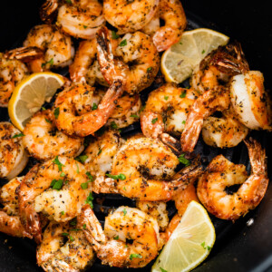 Seasoned air fried shrimp in an air fryer basket with lemon wedges.