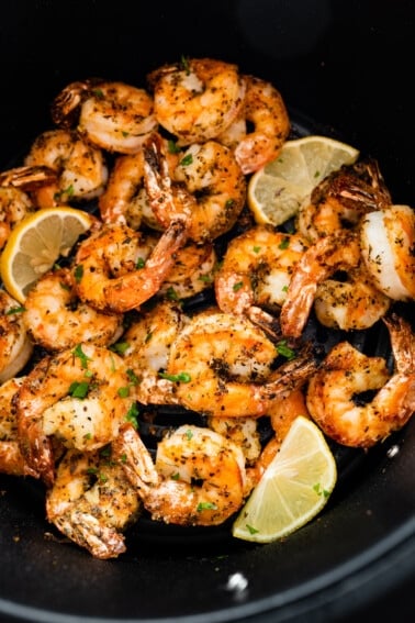 Seasoned air fried shrimp in an air fryer basket with lemon wedges.