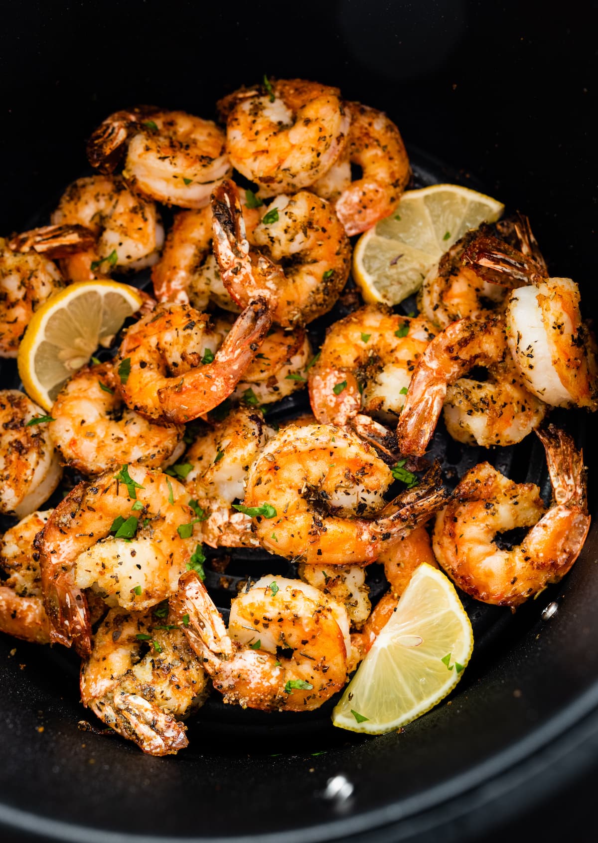 Seasoned air fried shrimp in an air fryer basket with lemon wedges.