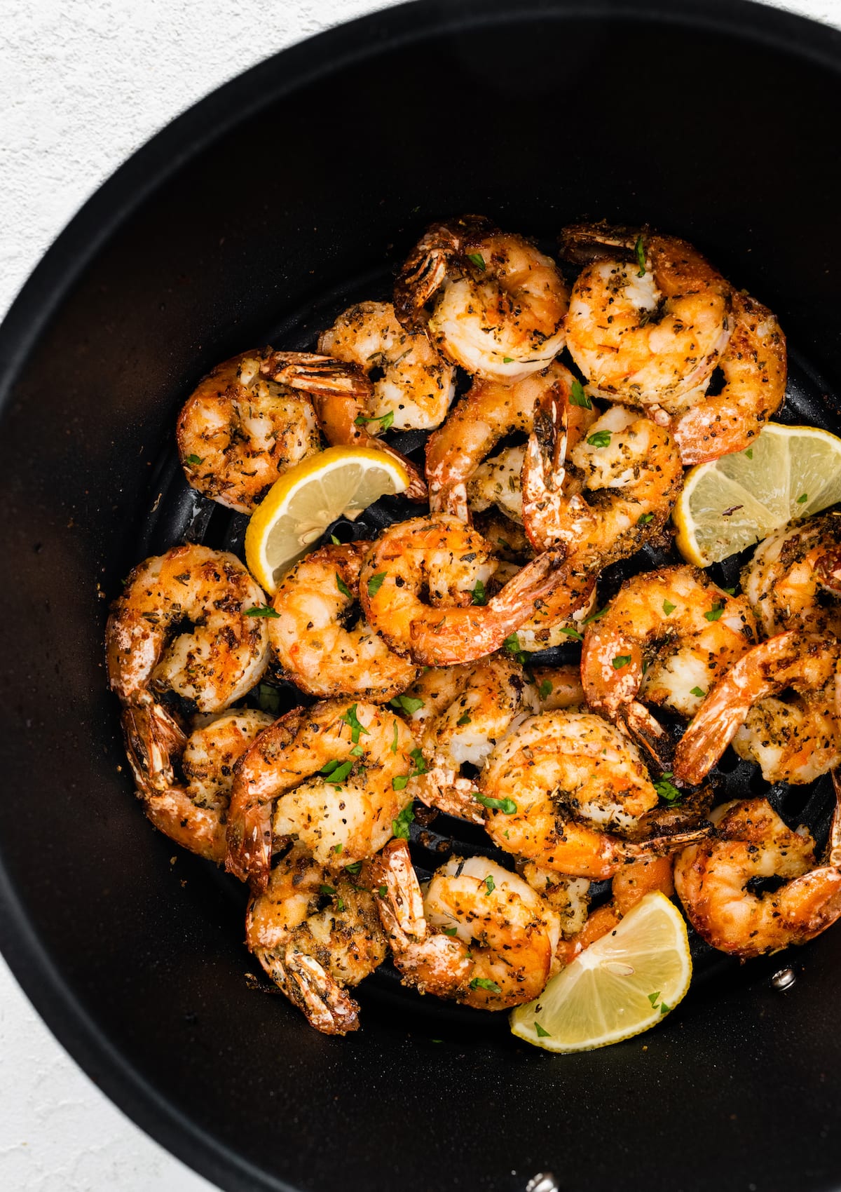 Seasoned air fried shrimp in an air fryer basket with lemon wedges.