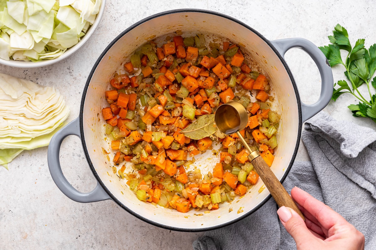A tablespoon of apple cider vinegar being added to a large pot of diced vegetables.