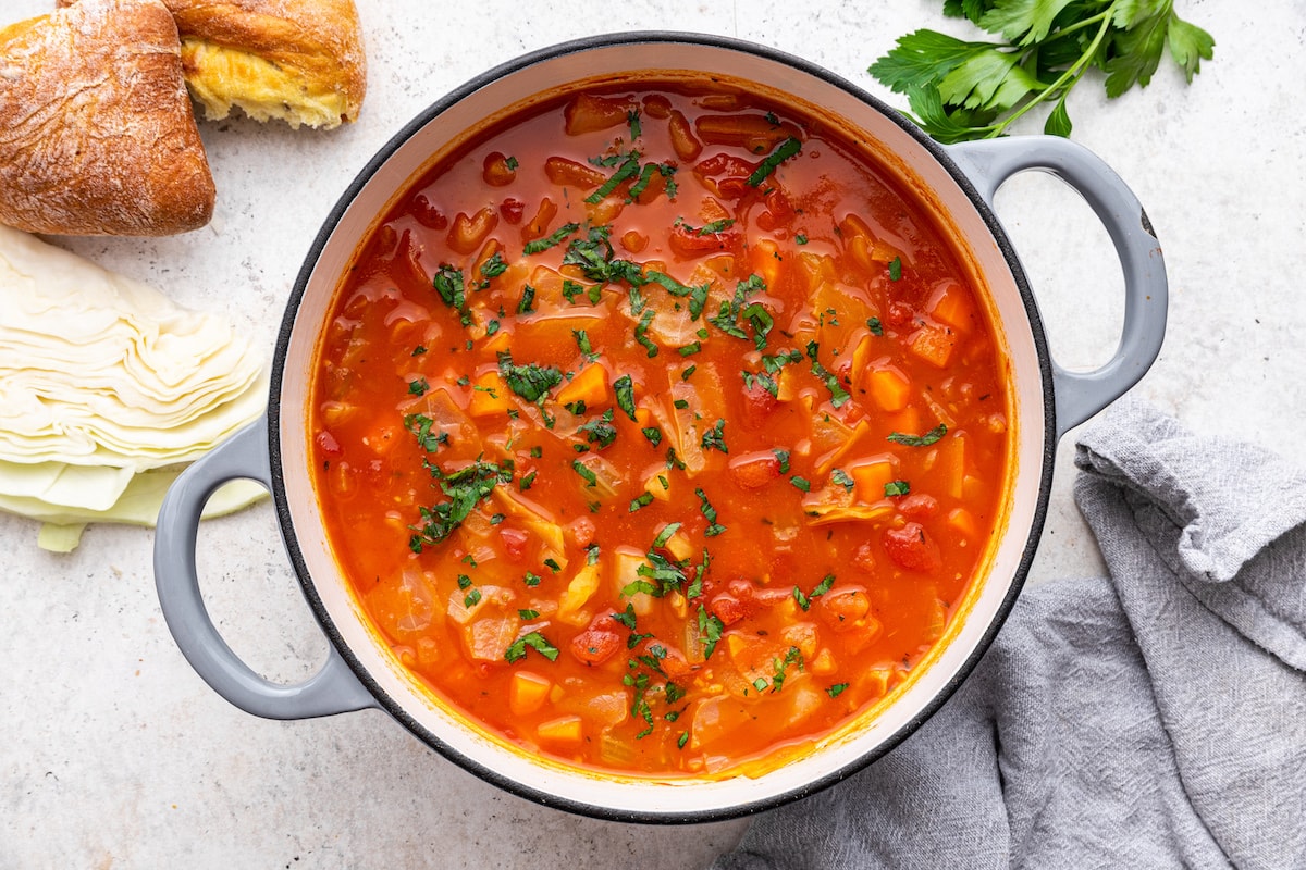 Cabbage soup in a large pot garnished with fresh herbs.