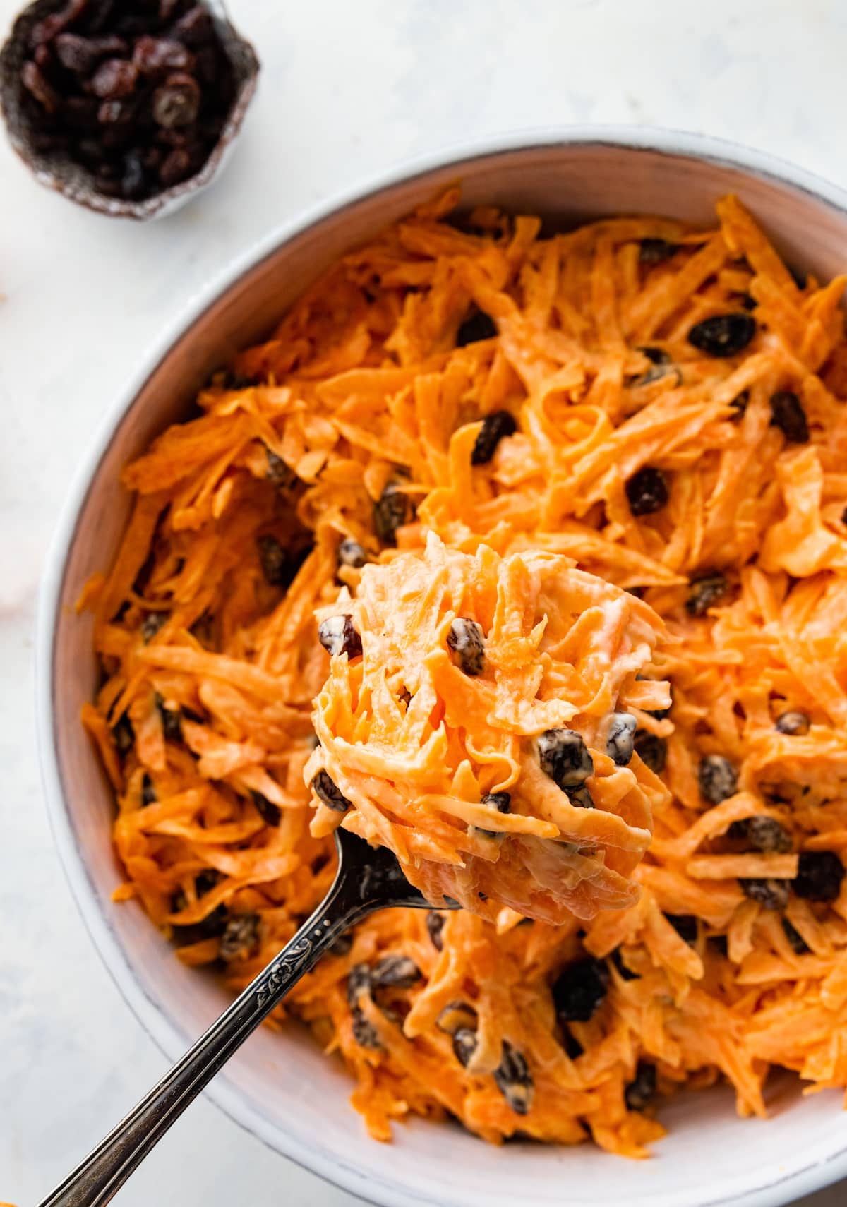 A carrot raisin salad in a white bowl with a spoon.